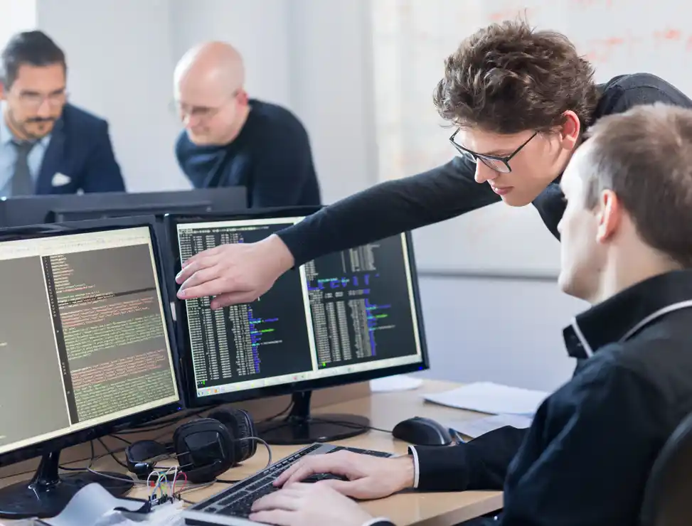 Szene mit Dozent und Schüler vor einem Computer am Arbeitsplatz